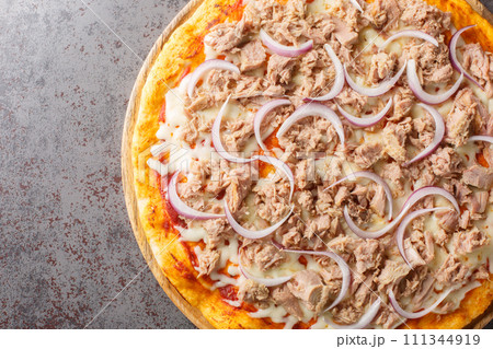 Mediterranean traditional Pizza Tuna with tomato sauce, canned tuna, mozzarella cheese and red onion close-up on a wooden board. Horizontal top view Mediterranean traditional Pizza Tuna with tomato sauce, canned tuna, mozzarella cheese and red onion close-up on a wooden board. Horizontal top view 111344919