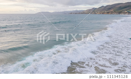 As the sun sets, Pismo Beach transforms into an enchanting winter wonderland with an empty, expansive sandy shore, bathed in golden hues, and the soothing sounds of the waves creating a tranquil 111345128