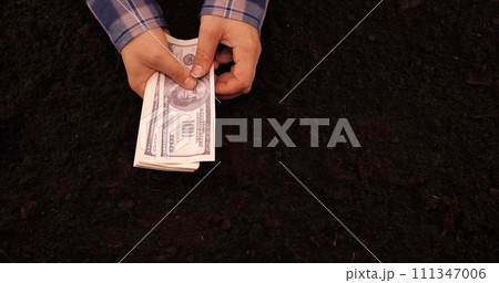 A farmer counts money in his hands against the background of soil The farmer calculates the income from the sale of the prepared crop Counting banknotes against the background of the earth, top view. A farmer counts money in his hands against the background of soil The farmer calculates the income from the sale of the prepared crop Counting banknotes against the background of the earth, top view. 111347006
