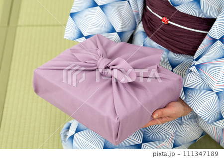 和室の畳に座って紫色の風呂敷包みを持つ浴衣姿のミドル女性 111347189
