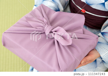 和室の畳に座って紫色の風呂敷包みを持つ浴衣姿のミドル女性 111347243