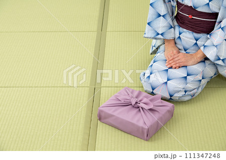 和室の畳に座って紫色の風呂敷包みを持つ浴衣姿のミドル女性 111347248