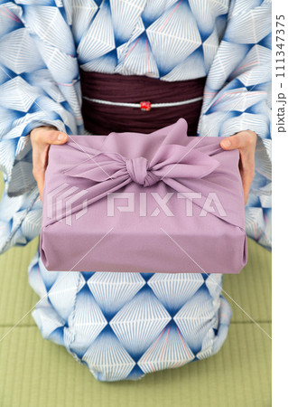 和室の畳に座って紫色の風呂敷包みを持つ浴衣姿のミドル女性 111347375