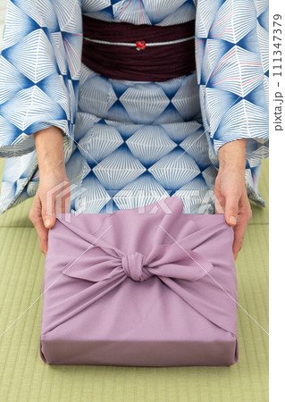 和室の畳に座って紫色の風呂敷包みを持つ浴衣姿のミドル女性 111347379