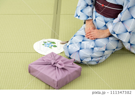 和室の畳に座って紫色の風呂敷包みを持つ浴衣姿のミドル女性 111347382