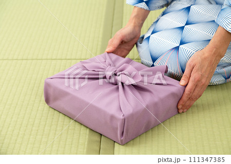 和室の畳に座って紫色の風呂敷包みを持つ浴衣姿のミドル女性 111347385
