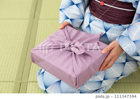 和室の畳に座って紫色の風呂敷包みを持つ浴衣姿のミドル女性 111347394