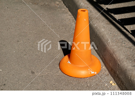 A traffic orange cone is used as a barrier during road construction work A traffic orange cone is used as a barrier during road construction work 111348008