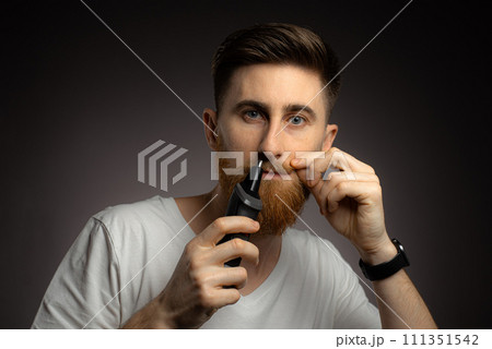 A young guy uses a nose trimmer to remove nose hair 111351542
