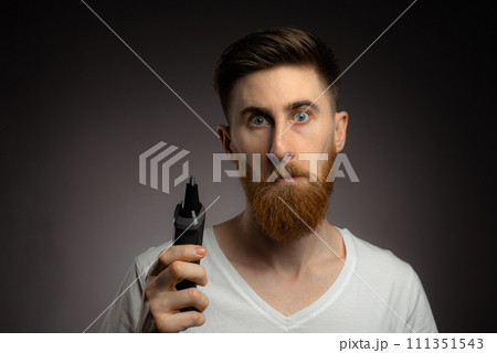 A young guy uses a nose trimmer to remove nose hair A young guy uses a nose trimmer to remove nose hair 111351543