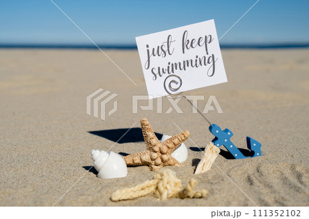 JUST KEEP SWIMMING text on paper greeting card in anchor paper holder and starfish seashell summer vacation decor. Sandy beach sun coast. Holiday concept postcard. Getting away Travel JUST KEEP SWIMMING text on paper greeting card in anchor paper holder and starfish seashell summer vacation decor. Sandy beach sun coast. Holiday concept postcard. Getting away Travel 111352102