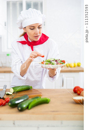 Portrait of woman chef decorating salad Portrait of woman chef decorating salad 111352593