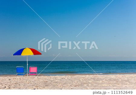 Colorful Umbrella with Pink and Blue Deckchairs on an Empty Beach 111352649