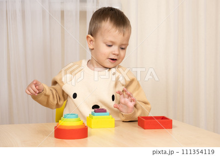 Little boy playing with wooden multicolored Montessori toys. 111354119