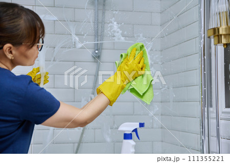 Woman cleaning bathroom, washing glass in shower Woman cleaning bathroom, washing glass in shower 111355221