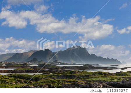 Jagged peaks tower over sea in Andenes, Lofoten Islands, under sky with fluffy clouds 111356077