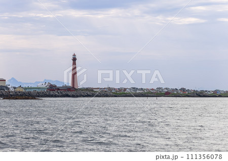 Towering red lighthouse, Andenes beacon, above calm sea 111356078