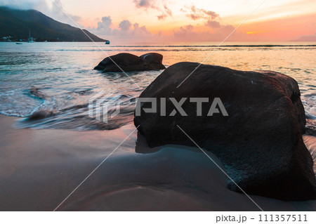 Coastal landscape with wet sand and silhouettes of rocks at sunset Coastal landscape with wet sand and silhouettes of rocks at sunset 111357511