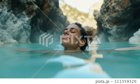 A woman basking in the warm embrace of a natural hot spring, surrounded by towering cliffs A woman basking in the warm embrace of a natural hot spring, surrounded by towering cliffs 111359320