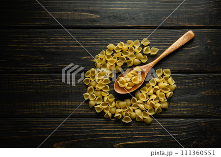 Shell-type pasta on an antique dark table and in a spoon before preparing breakfast. Space for a recipe or menu for a restaurant 111360551