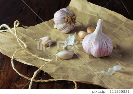 Garlic bulbs on packing paper, on rustic wooden table. Closeup garlic Garlic bulbs on packing paper, on rustic wooden table. Closeup garlic 111360821