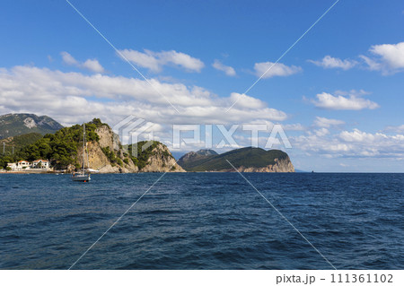 View of a sea and sailing boat with hills and blue sky with white fluffy clouds in background 111361102