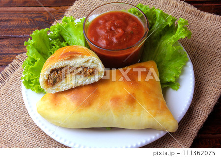 meat esfiha (sfiha) of Arab origin traditionally adapted for the Brazilian cuisine on plate on rustic wooden table meat esfiha (sfiha) of Arab origin traditionally adapted for the Brazilian cuisine on plate on rustic wooden table 111362075