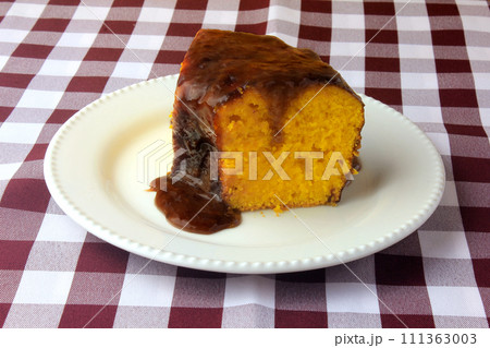 slice of carrot cake with chocolate coating on white ceramic plate on rustic wooden table 111363003