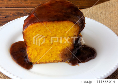 slice of carrot cake with chocolate coating on white ceramic plate on rustic wooden table 111363014