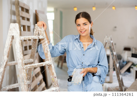 Portrait of positive young woman next to a stepladder in renovated room 111364261