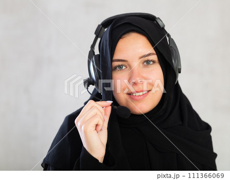 Happy young woman dressed in traditional islamic clothes with headphones with microphone on 111366069