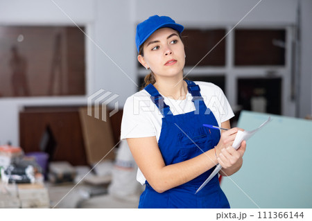 Woman in blue overalls checks the completed construction work on drawing 111366144
