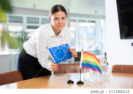 Young woman puts EU and LGBT flags on table in office Young woman puts EU and LGBT flags on table in office 111366222