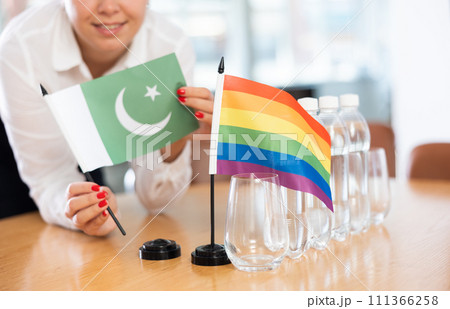 Young woman puts Pakistani and LGBT flags on table in office 111366258