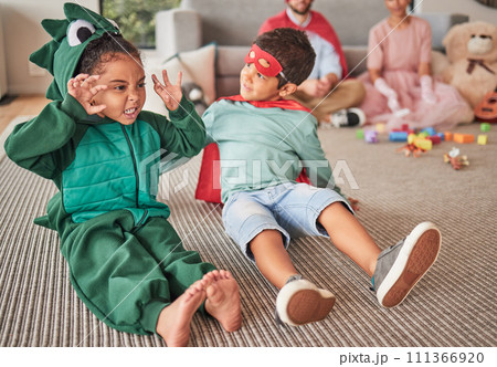 Family, halloween and children playing in costume on a floor in a living room, having fun and being creative. Superhero, dinosaur and creative kids bonding in character, excited and happy together 111366920