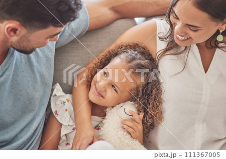 Love, family and girl bonding on a sofa with her parents, loving and caring in a living room at home. Happy, relax and smiling mother and father embracing their daughter, enjoy moment of parenthood 111367005