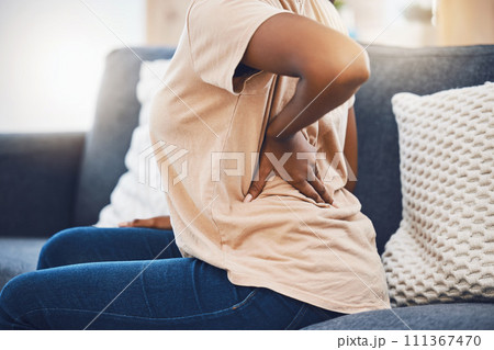 Woman with a back injury, pain or accident from stress sitting on sofa in her living room. Black girl with a muscle sprain, back pain or injured spine medical emergency on couch in lounge at home. 111367470