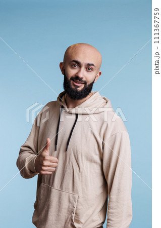 Smiling arab man expressing satisfaction with thumb up gesture portrait. Young happy handsome person with carefree emotions showing approval and agreement while looking at camera 111367759