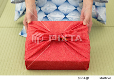 和室の畳に座って赤い風呂敷包みを持つ浴衣姿のミドル女性 111368658