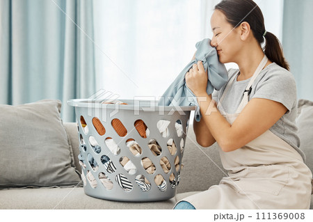Woman on sofa smell clean laundry at home, in living room while cleaning or doing housekeeping. Lady smile on couch with washing basket in lounge, sniff fresh fabric or clothes in house. Woman on sofa smell clean laundry at home, in living room while cleaning or doing housekeeping. Lady smile on couch with washing basket in lounge, sniff fresh fabric or clothes in house. 111369008