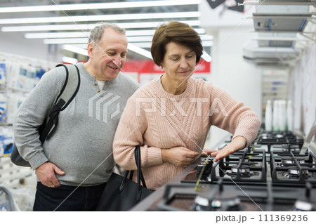 Mature man and woman choosing gas stove in appliance shop Mature man and woman choosing gas stove in appliance shop 111369236