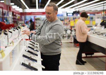 Aged man choosing digital wristwatches in electronic store Aged man choosing digital wristwatches in electronic store 111369240