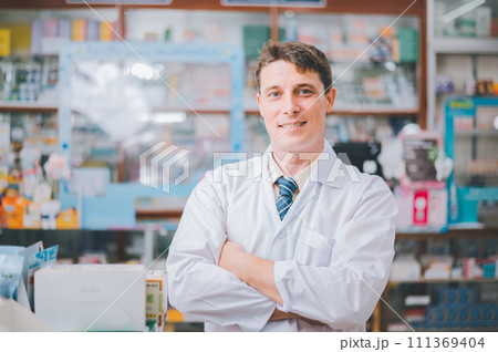 Male pharmacist posing confidently welcoming, advising patients and prescription patients in modern pharmacy. Male pharmacist posing confidently welcoming, advising patients and prescription patients in modern pharmacy. 111369404