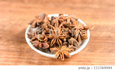 anise stars in a white bowl on wooden table 111369994