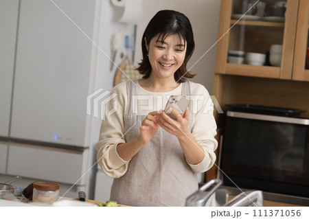 料理をしながらスマホを見る女性・笑顔の主婦 111371056