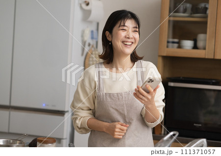 料理をしながらスマホを見る女性・笑顔の主婦 料理をしながらスマホを見る女性・笑顔の主婦 111371057