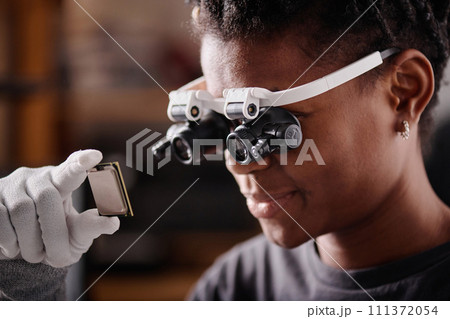African american electronic repairman in glasses holding CPU close to her face and examining it 111372054