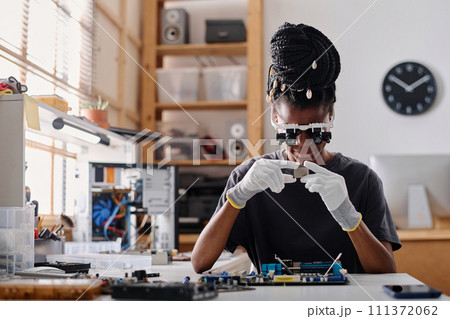 Female african american technician wearing glasses with binocular loupes attentively examining CPU 111372062
