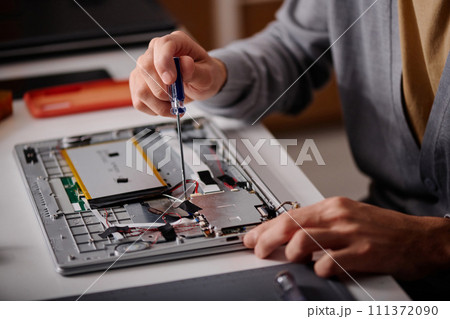Unrecognizable engineer using screwdriver repairing element of disassembled laptop 111372090