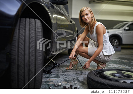 Woman, portrait and car jack for change tyre in parking garage for breakdown or wheel failure, puncture or maintenance. Female person, fashion and face with tools for vehicle, repair 111372387